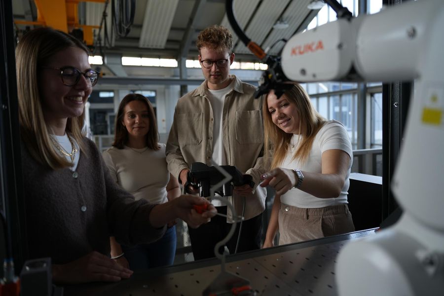 Gruppe steht vor einem Industrieroboter im Technikum und bedient ihn über ein Handbediengerät.